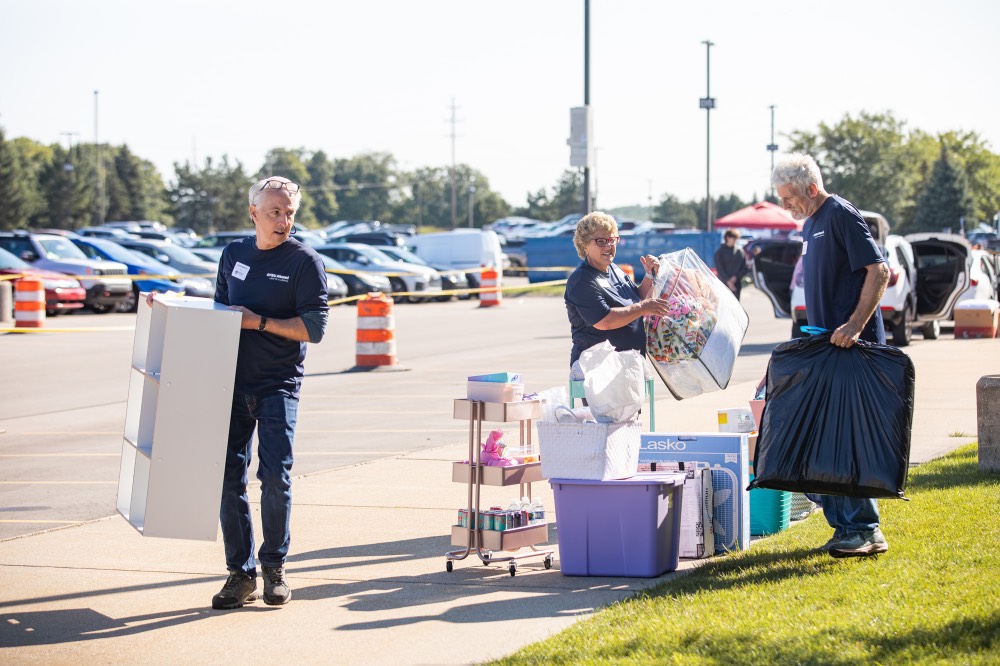 GVSU Alumni grabbing things from a pile and carrying it inside